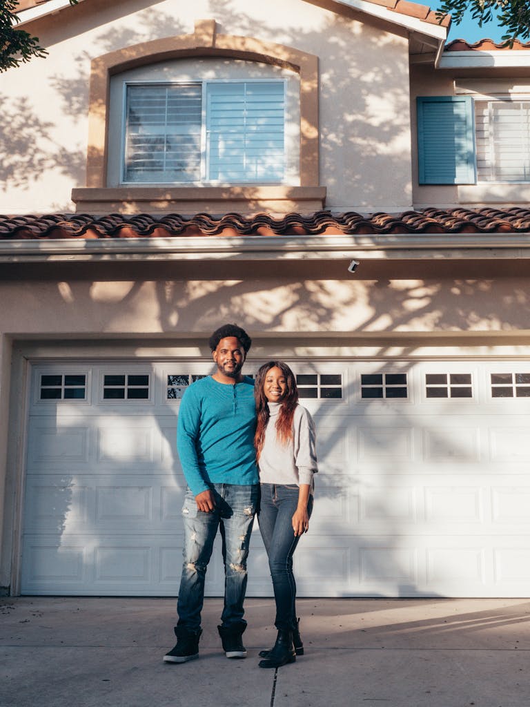A joyful couple stands in front of their new garage featuring an affordable door option improving their home value.