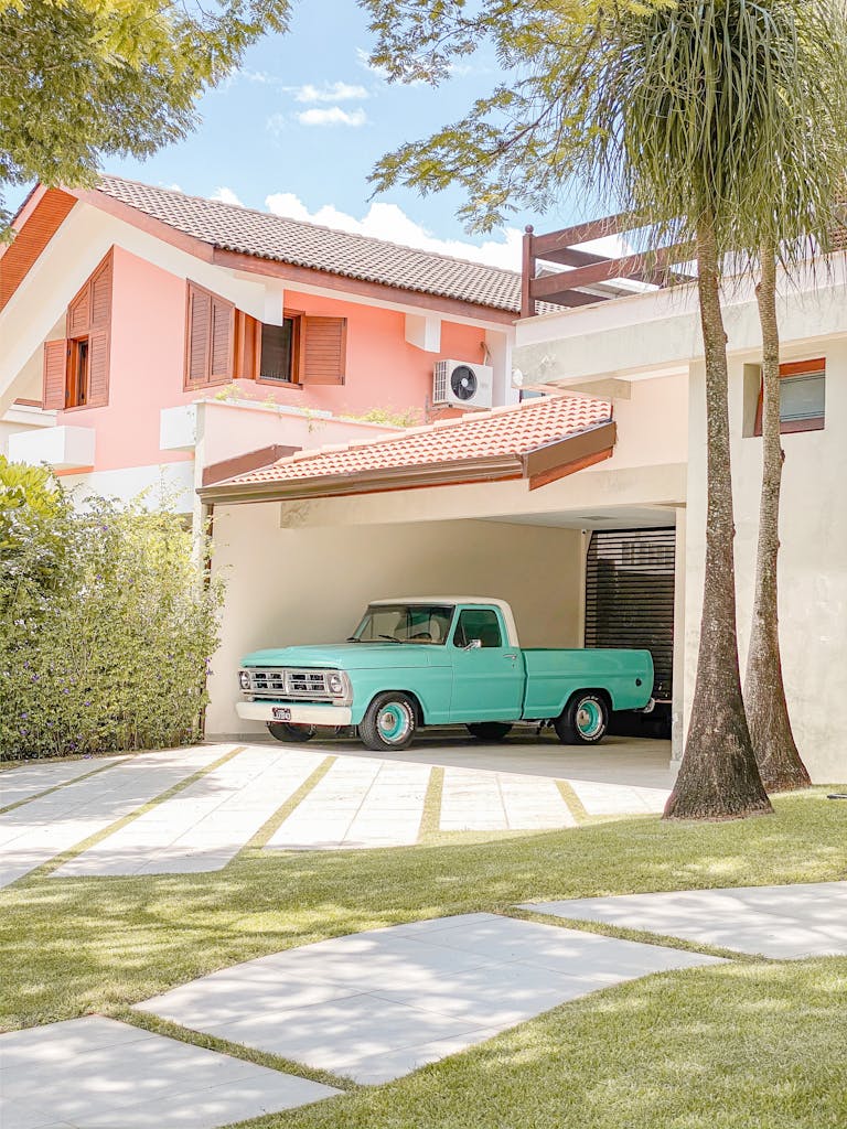 A teal vintage pickup truck parked in a suburban garage featuring a roll up door.