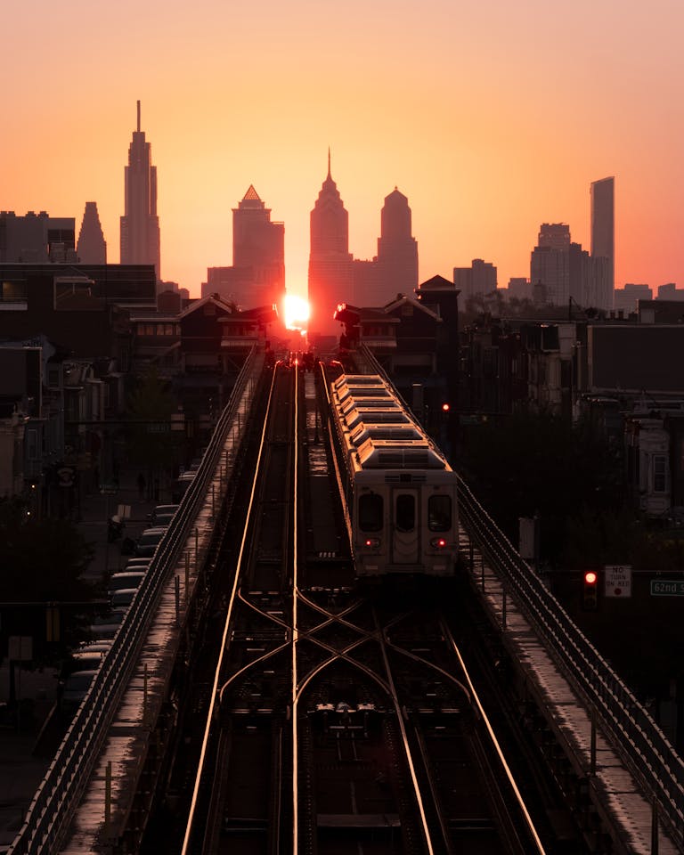 A train crosses a bridge during sunset with the Philadelphia skyline in the background.