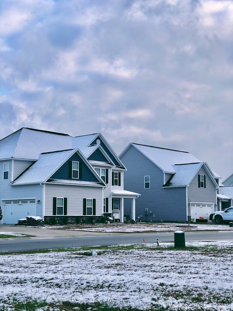 Charming suburban homes with multi car garages, with light snow on rooftops and ground, cloudy winter sky overhead.
