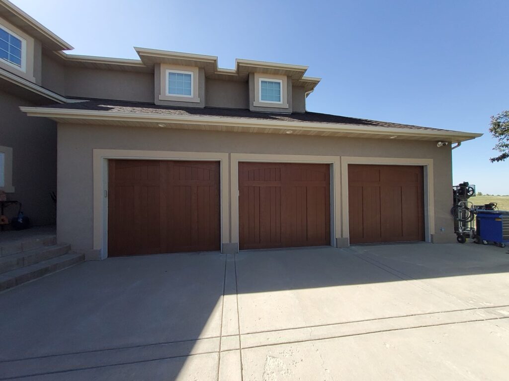 3 single car wooden garage doors featured on a large modern home.