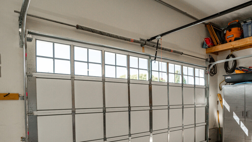 New garage door replacement seen form inside the garage, showing all new parts and panels with paned windows across the top.