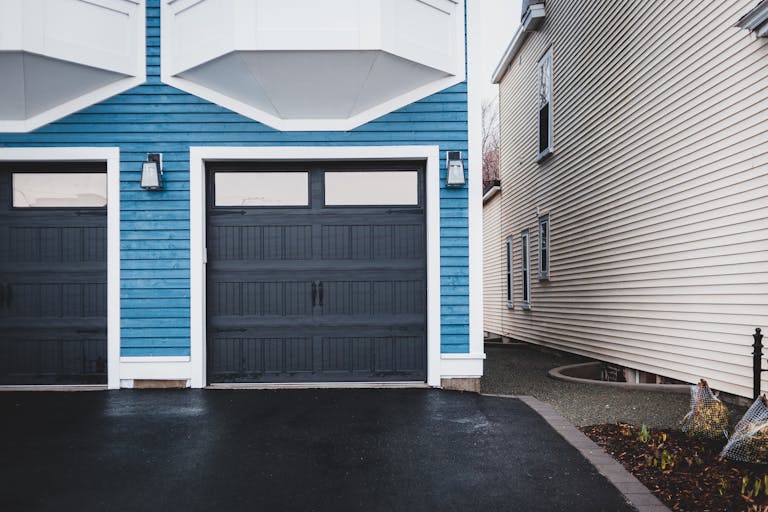 Elegant urban house exterior with blue facade and stylish garage doors that would be ideal for use with a jackshaft garage door opener.
