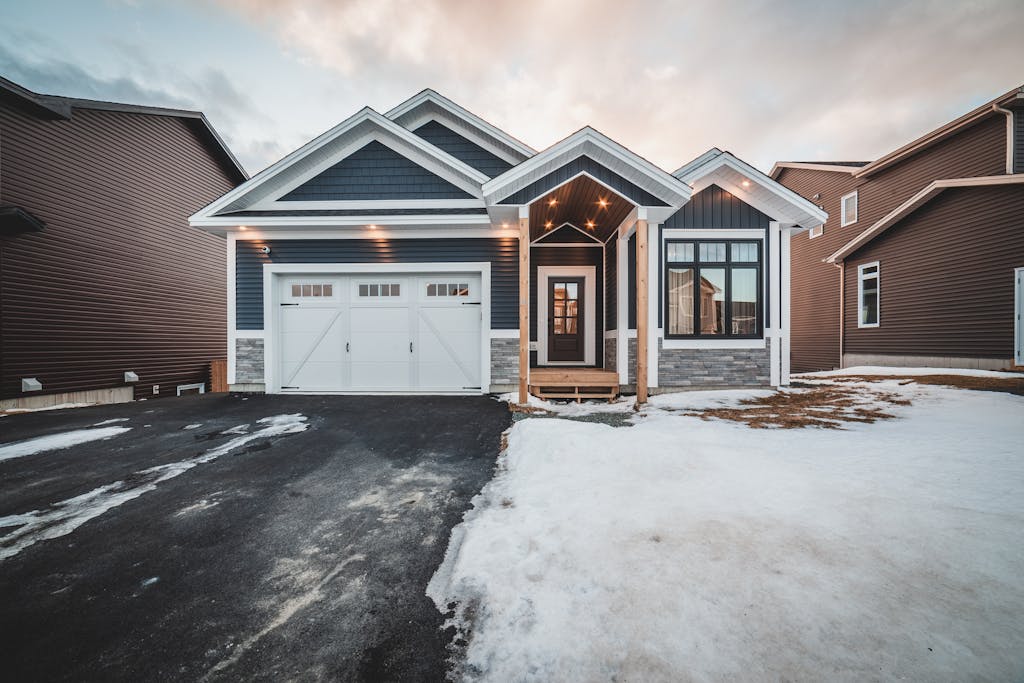 Exterior of modern blue cottage house with custom style garage door and snow in daylight