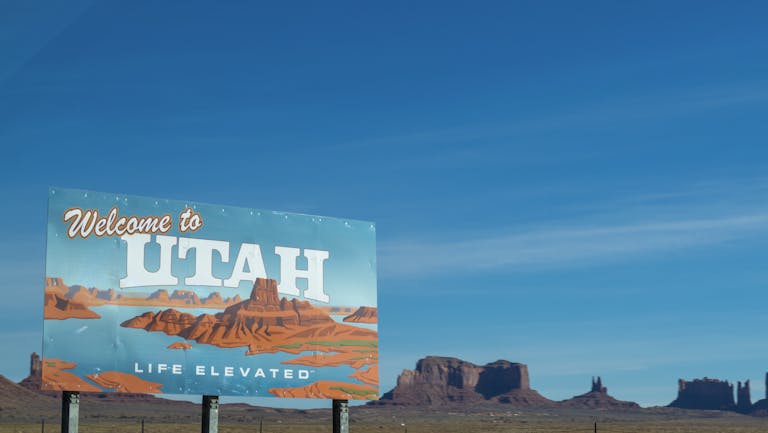 Scenic view of Utah welcome sign against desert and blue sky backdrop.