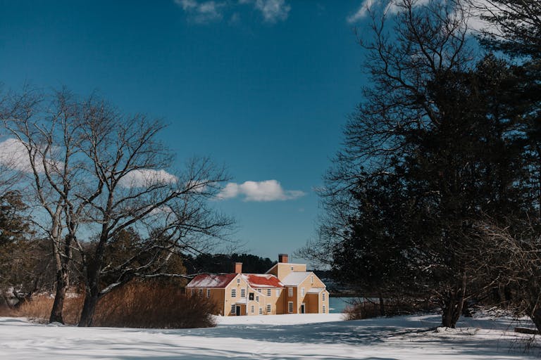 Winter scene with a quaint yellow house surrounded by snow and bare trees in New Hampshire.